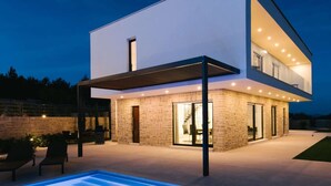 A modern two-story house with a swimming pool in the foreground.