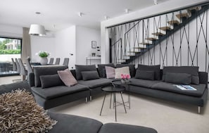 Un salon moderne avec un canapé d’angle, une table basse ronde et un escalier doté d’une rampe au design original.
