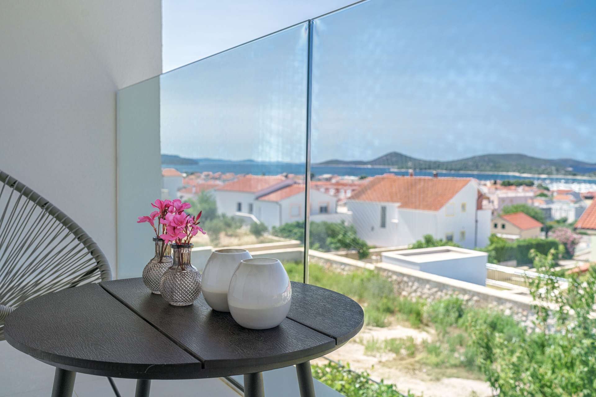A balcony with a table, two vases, and a chair.