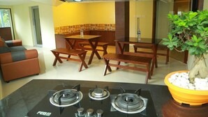 A modern kitchen with a gas stove, wooden dining table, and chairs. - Hotel Brahmaputhra (Chavakkad)