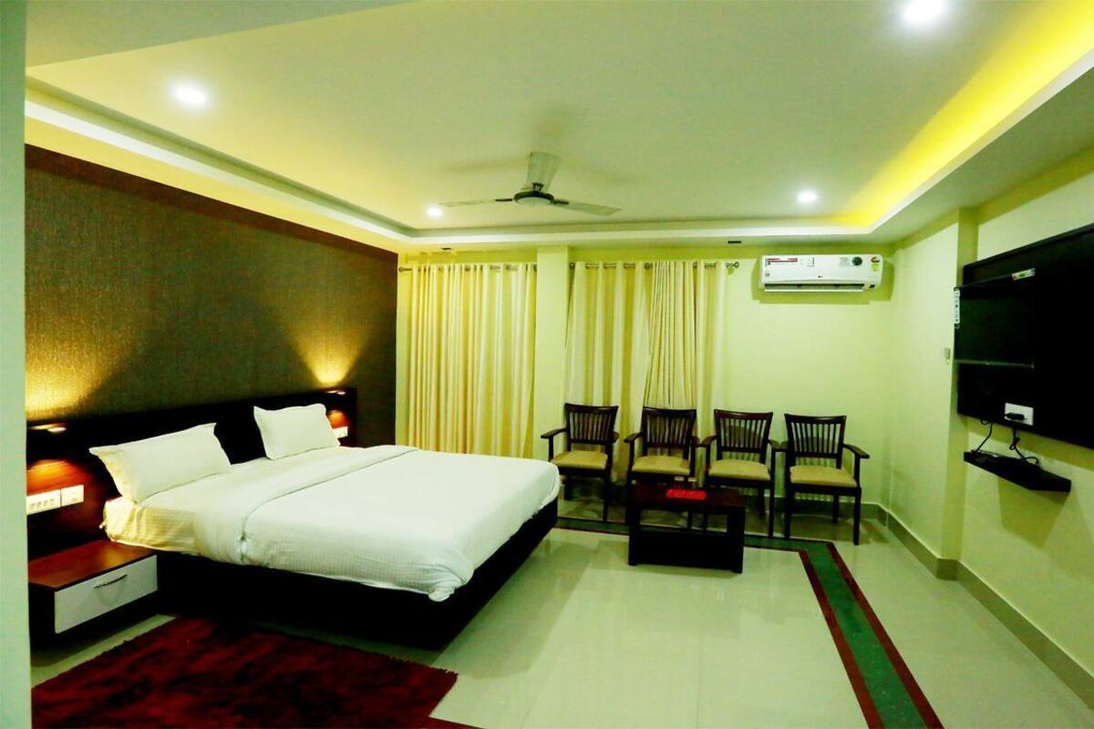 A hotel room with a bed, a TV, a ceiling fan, and a seating area with chairs.