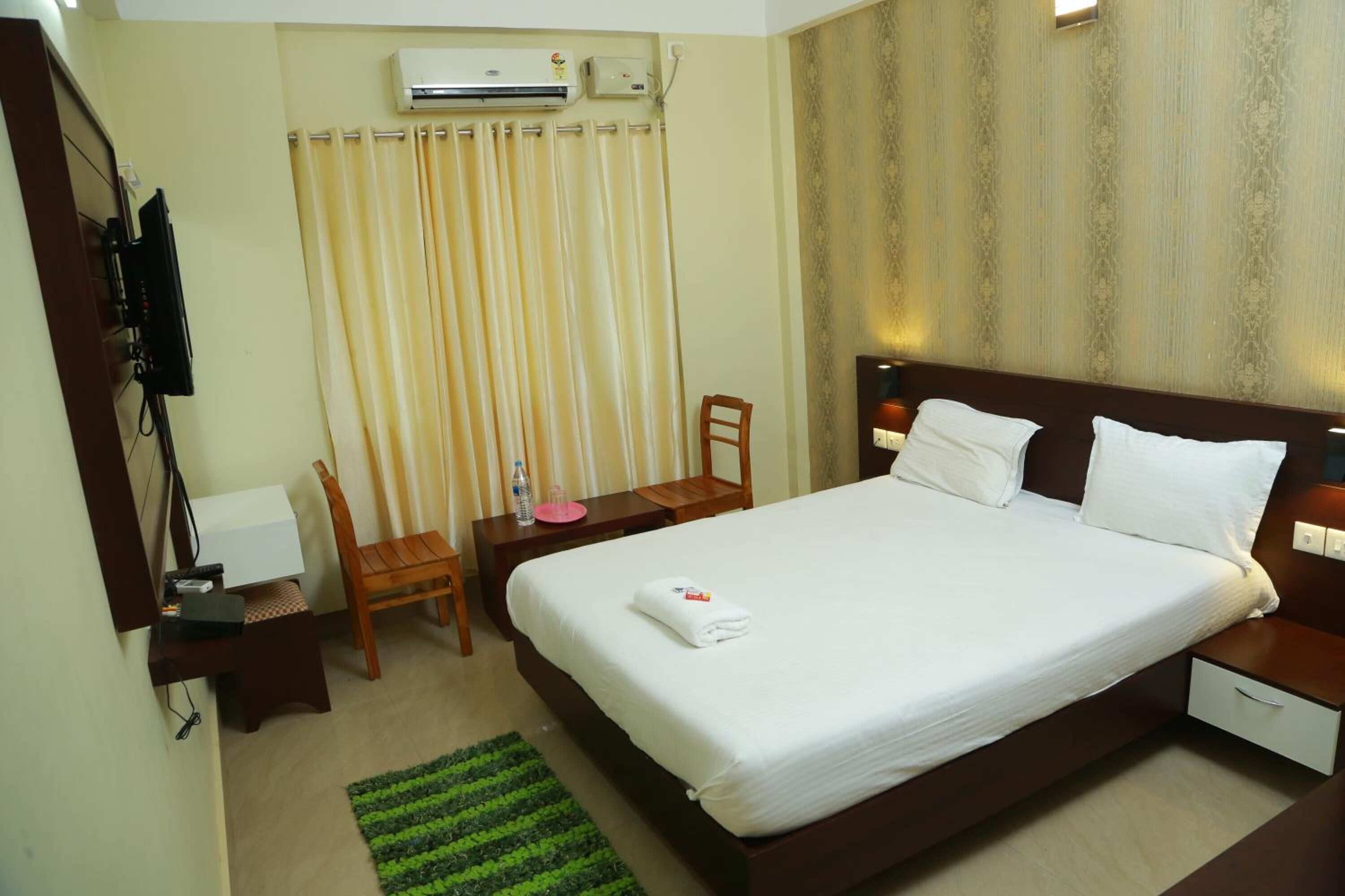 Habitación de hotel con cama, escritorio, silla, mesita pequeña, alfombra verde y cortina.