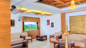 A modern living room with wooden furniture, a large TV, and a decorative wall piece. - Hotel Brahmaputhra (Chavakkad)