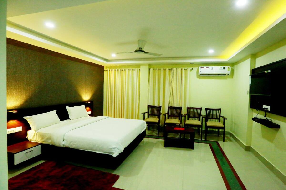 A hotel room with a bed, a desk, a chair, a TV, and an air conditioning unit.