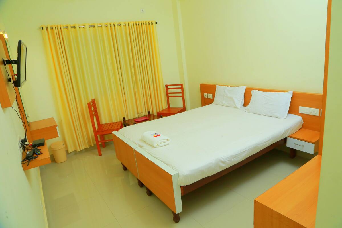 A hotel room with a single bed, a chair, a small table, and a TV mounted on the wall.