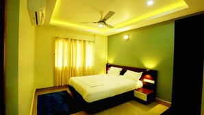 A hotel room with a bed, bedside table, nightstand, and ceiling fan. - Hotel Brahmaputhra (Chavakkad)