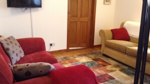 A living room with a red sofa, beige sofa, and a television mounted on the wall. - North End Nairn The Cottage (Nairn)