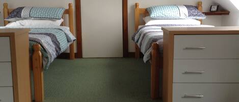 Una habitación con dos camas de madera, un tocador blanco y una alfombra verde.