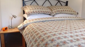 A neatly made bed with floral bedding, a bedside lamp, and a nightstand with a clock. - North End Nairn The Cottage (Nairn)