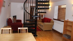 A living room with a wooden dining table, two red sofas, a beige sofa, a black spiral staircase, and a wooden bookshelf. - North End Nairn The Cottage (Nairn)