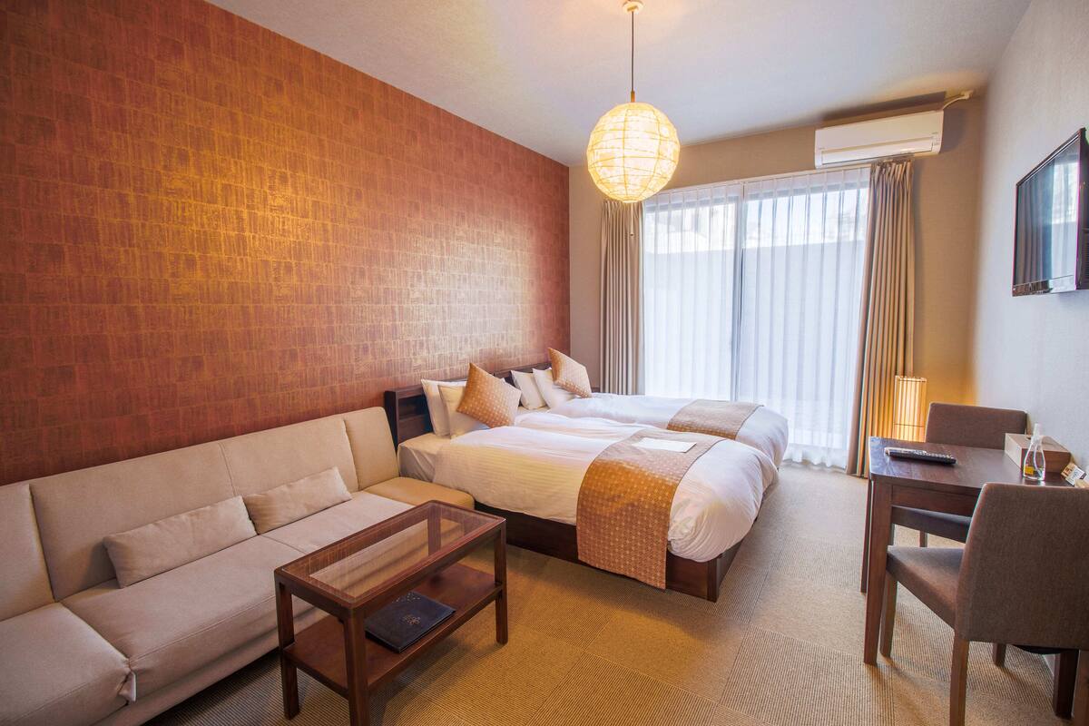A hotel room with a large bed, a sofa, a small table, and a TV.