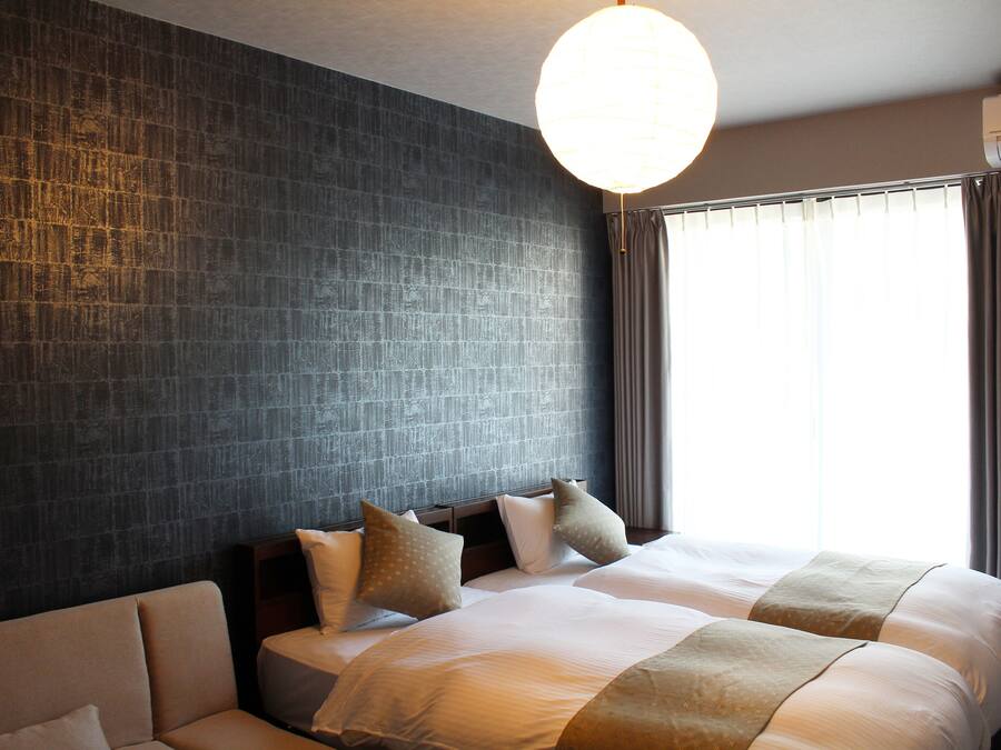 Habitació d'hotel amb un llit gran, un sofà, una paret amb textura i una finestra amb cortines.