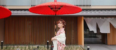 A woman standing in front of a building with a traditional Japanese entrance, wooden slats, and a tiled roof.