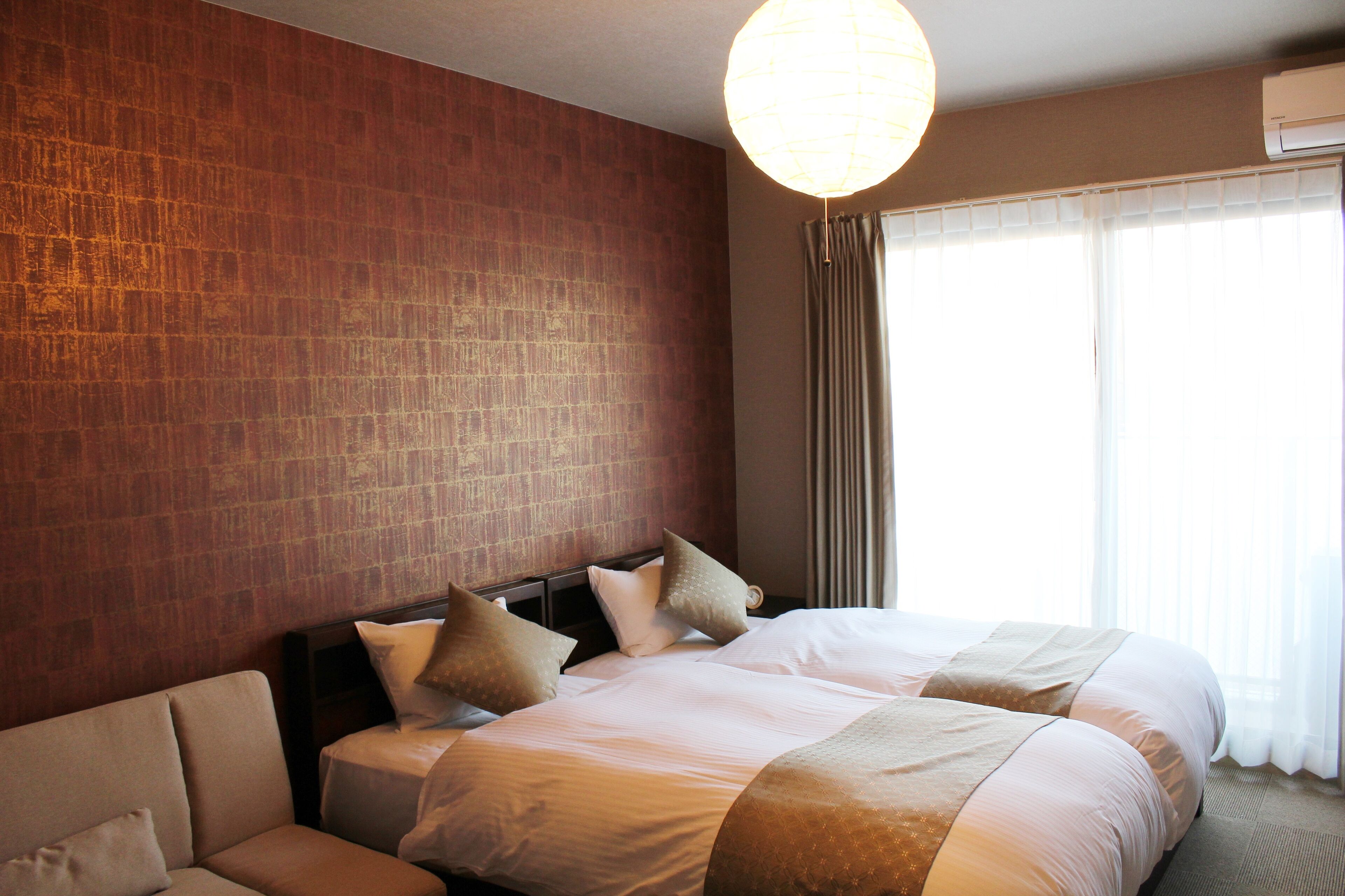 A hotel room with a large bed, a sofa, a brick-patterned wall, and a large window with curtains.
