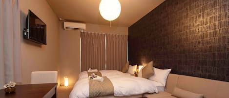 A hotel room with a bed, a sofa, a desk, and a wall-mounted TV.