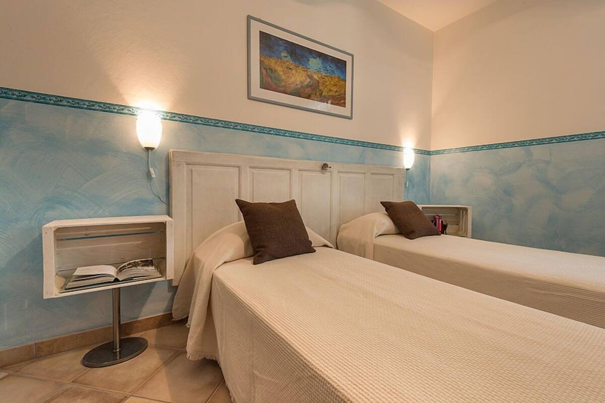 A hotel room with two single beds, a nightstand with a lamp, and a framed painting on the wall.