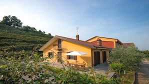 A yellow villa with a red roof, a patio with a table and chairs, and a view of a vineyard. - B&B Agrialpi (Bricherasio)