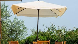 A patio with a table and chairs under a large umbrella, surrounded by greenery. - B&B Agrialpi (Bricherasio)