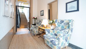 A hallway with a staircase leading to a room labeled 'pension Eden'. There are two patterned armchairs and a small table with a lamp and flowers. - Living Eden by we rent (Zell am See)