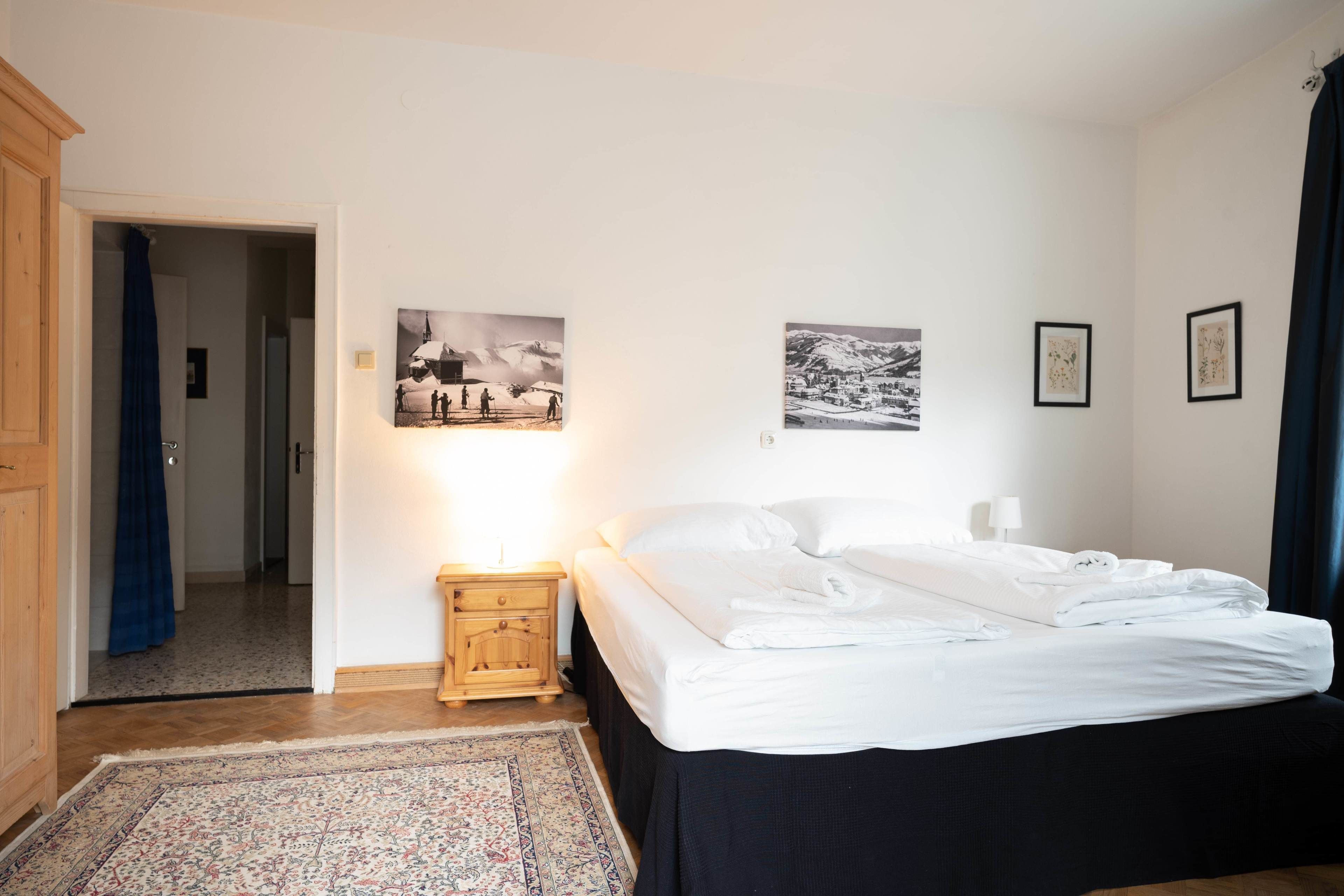 Un dormitorio con cama, mesita de noche, armario de madera y puerta que da a otra habitación.