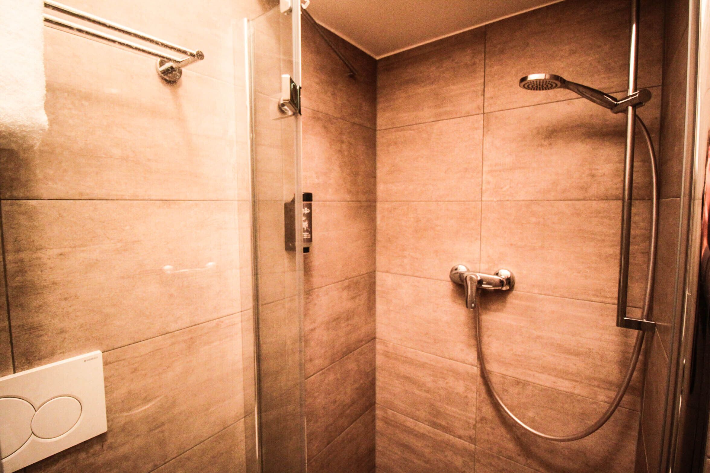 A modern bathroom with a glass shower enclosure, a handheld showerhead, and a wall-mounted faucet.