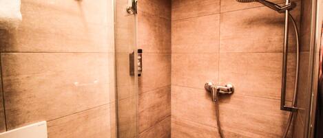 A modern bathroom with a glass shower enclosure, a handheld showerhead, and a wall-mounted faucet.