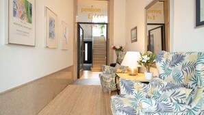A hallway with framed artwork, a sofa with a tropical print, a table with a lamp, and a staircase leading to another area. - Living Eden by we rent (Zell am See)