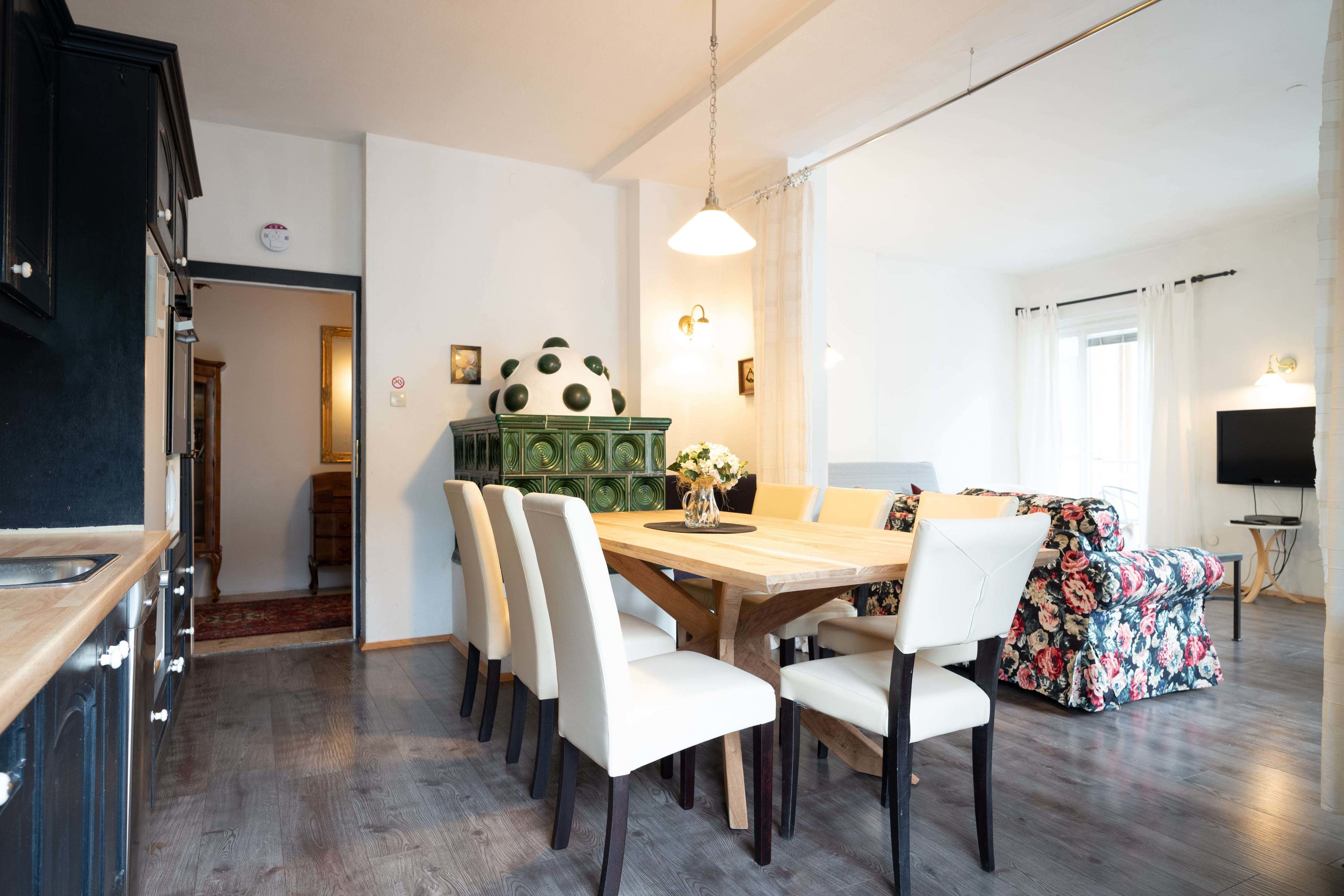 A dining area with a wooden table, white chairs, a green cabinet with a soccer ball, and a floral sofa.