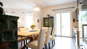 A dining area with a wooden table and white chairs, a dark green cabinet, and a hanging light fixture. - Living Eden by we rent (Zell am See)