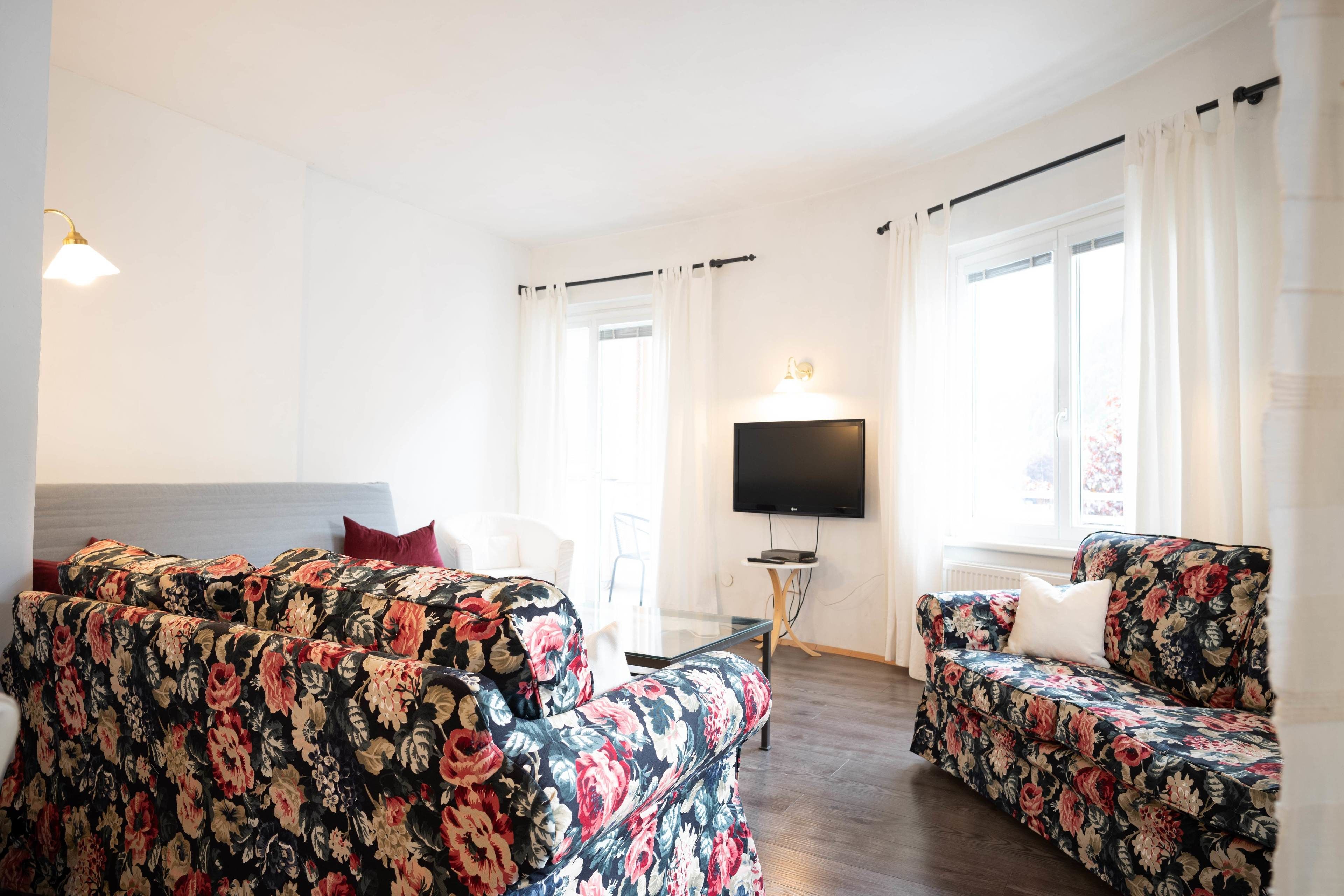 Ein Zimmer mit zwei blumigen Sofas, einem Flachbildfernseher und einem Bett mit Kopfteil.