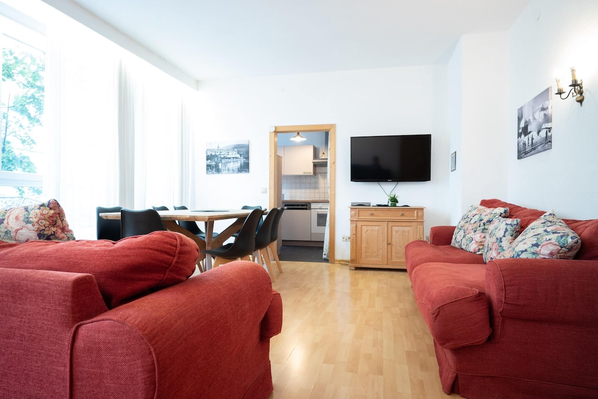 Una sala de estar con sofás rojos, televisor y un comedor con sillas y una mesa.