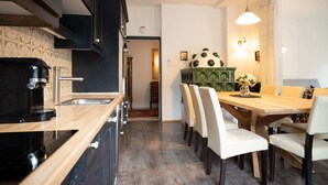 A modern kitchen with black cabinets, a wooden countertop, and a coffee machine. There is a dining area with a wooden table and white chairs. - Living Eden by we rent (Zell am See)