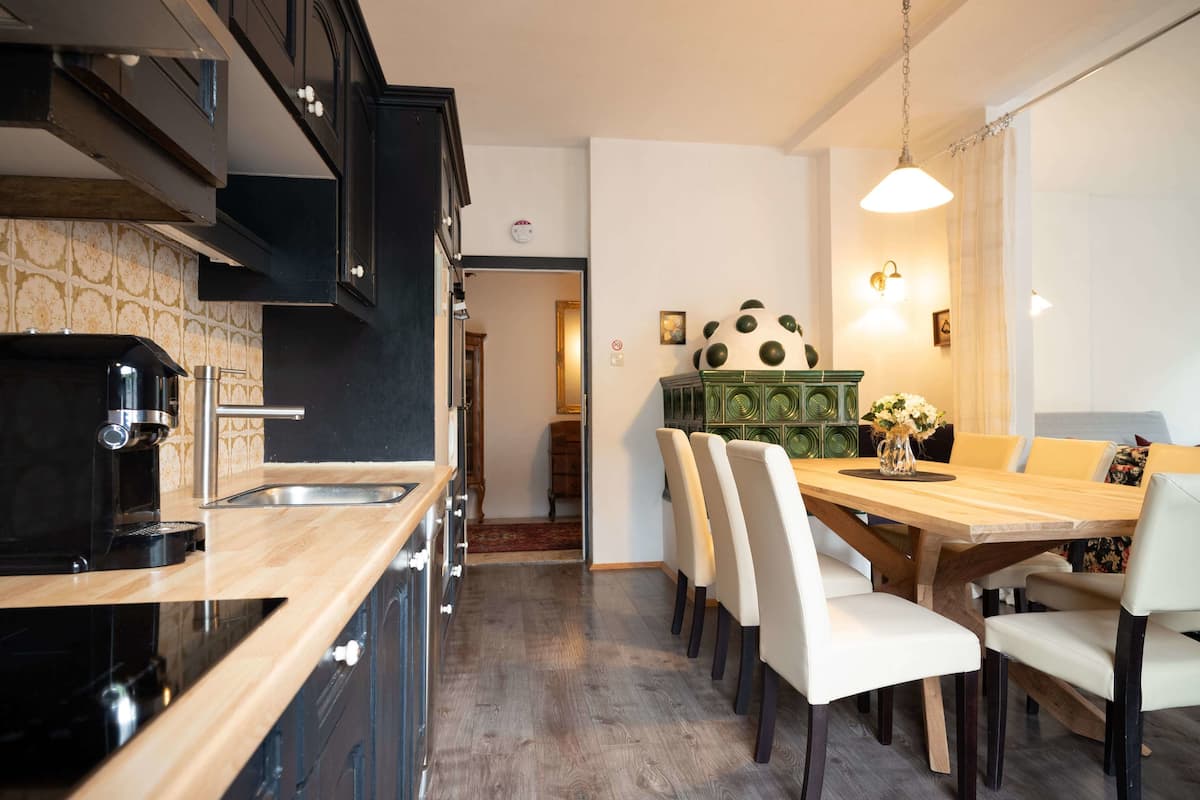 Una cocina moderna con armarios negros, encimera de madera y una cafetera. Hay una zona de comedor con una mesa de madera y sillas blancas.