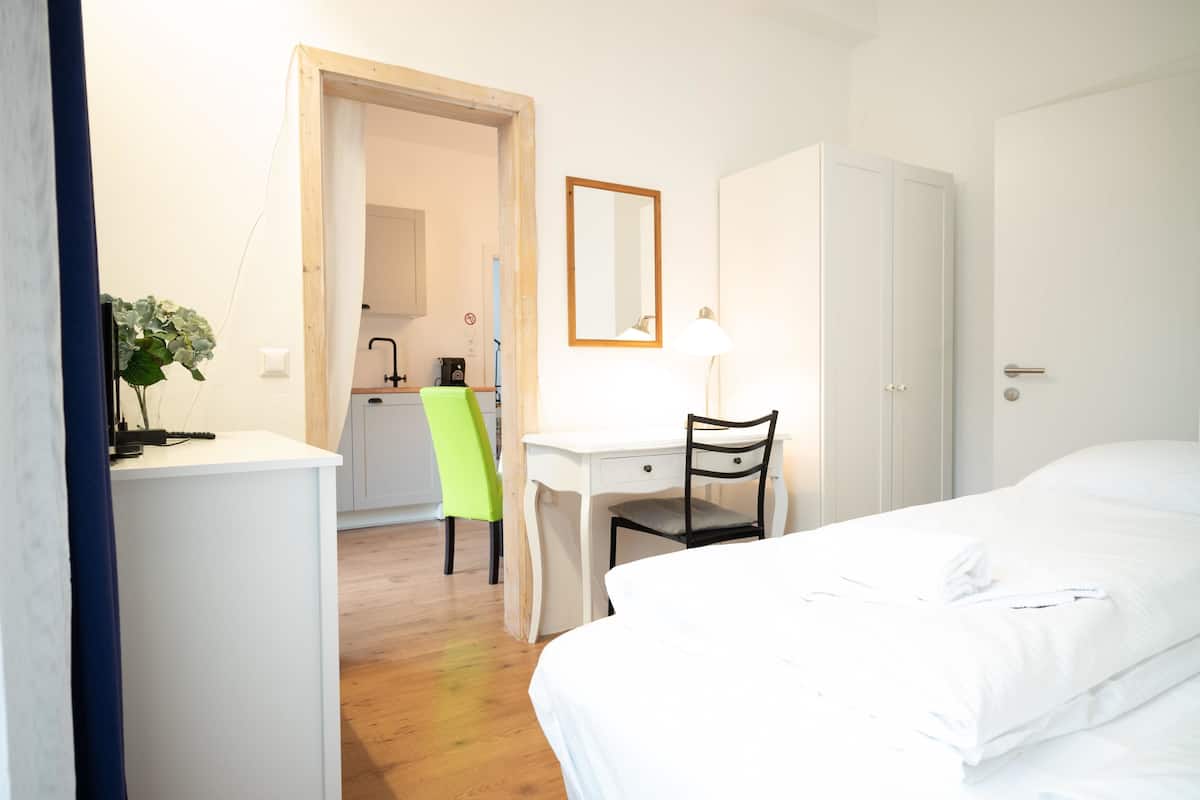Una habitación de hotel con cama, escritorio, silla, armario y una pequeña kitchenette.