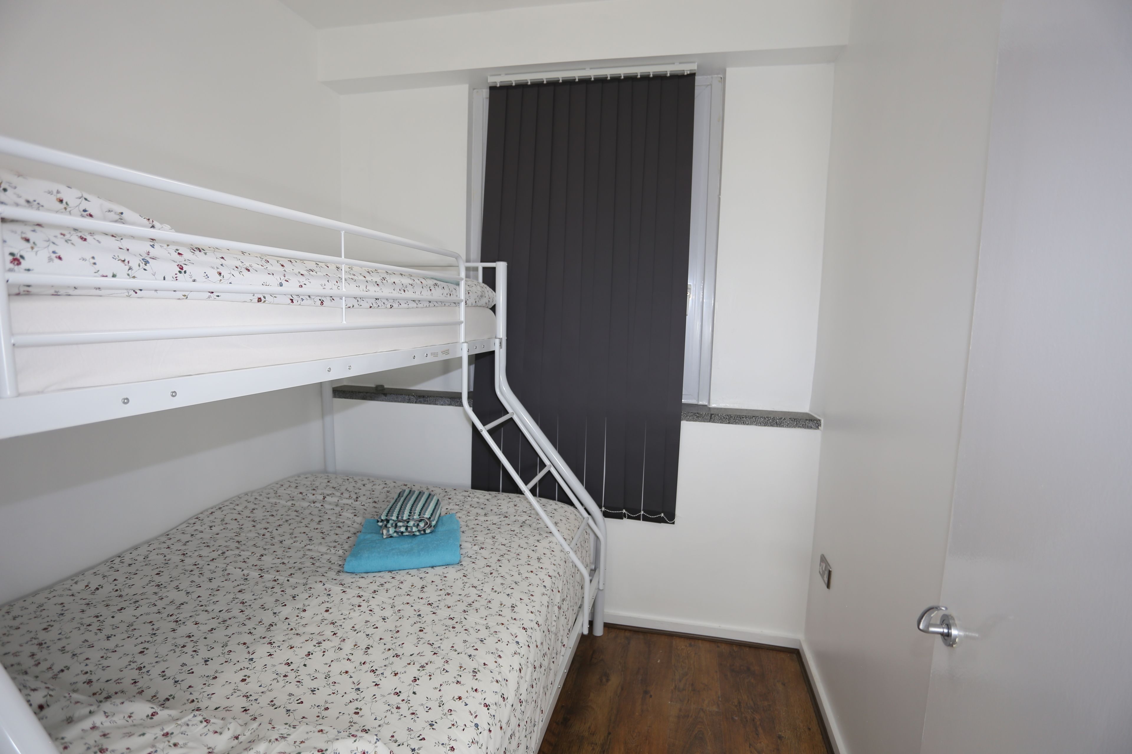 A bunk bed with a floral-patterned mattress, a blue towel, and a window with dark curtains.