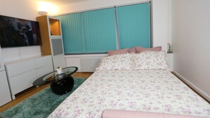 A bedroom with a bed, a TV, a small table, and a window with curtains.