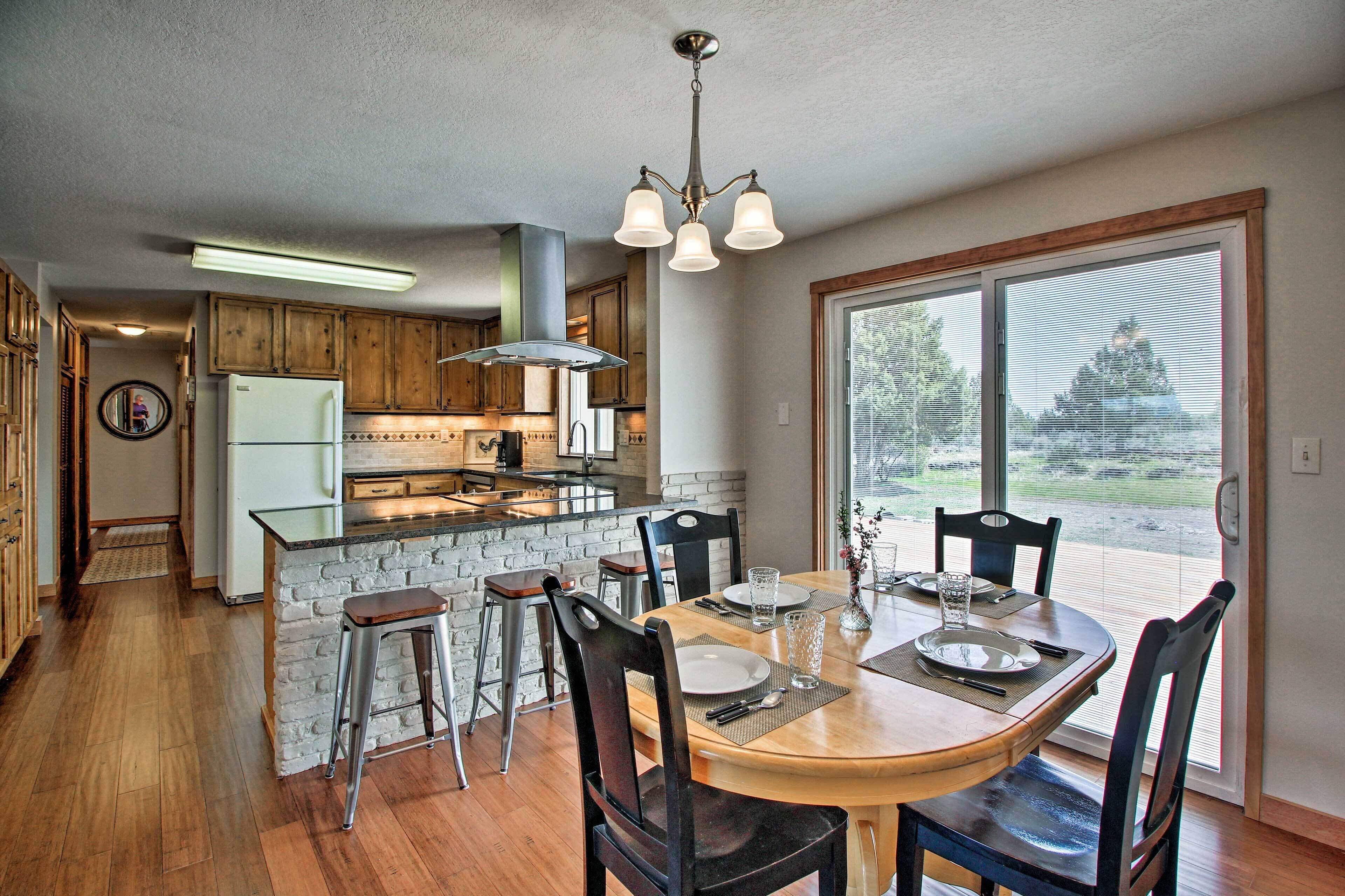 A modern kitchen with wooden cabinets, a central island, and a dining area with a large window.