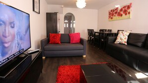 Ein modernes Wohnzimmer mit Flachbildfernseher, einem grauen Sofa mit roten Kissen, einem schwarzen Couchtisch und einem roten Teppich.