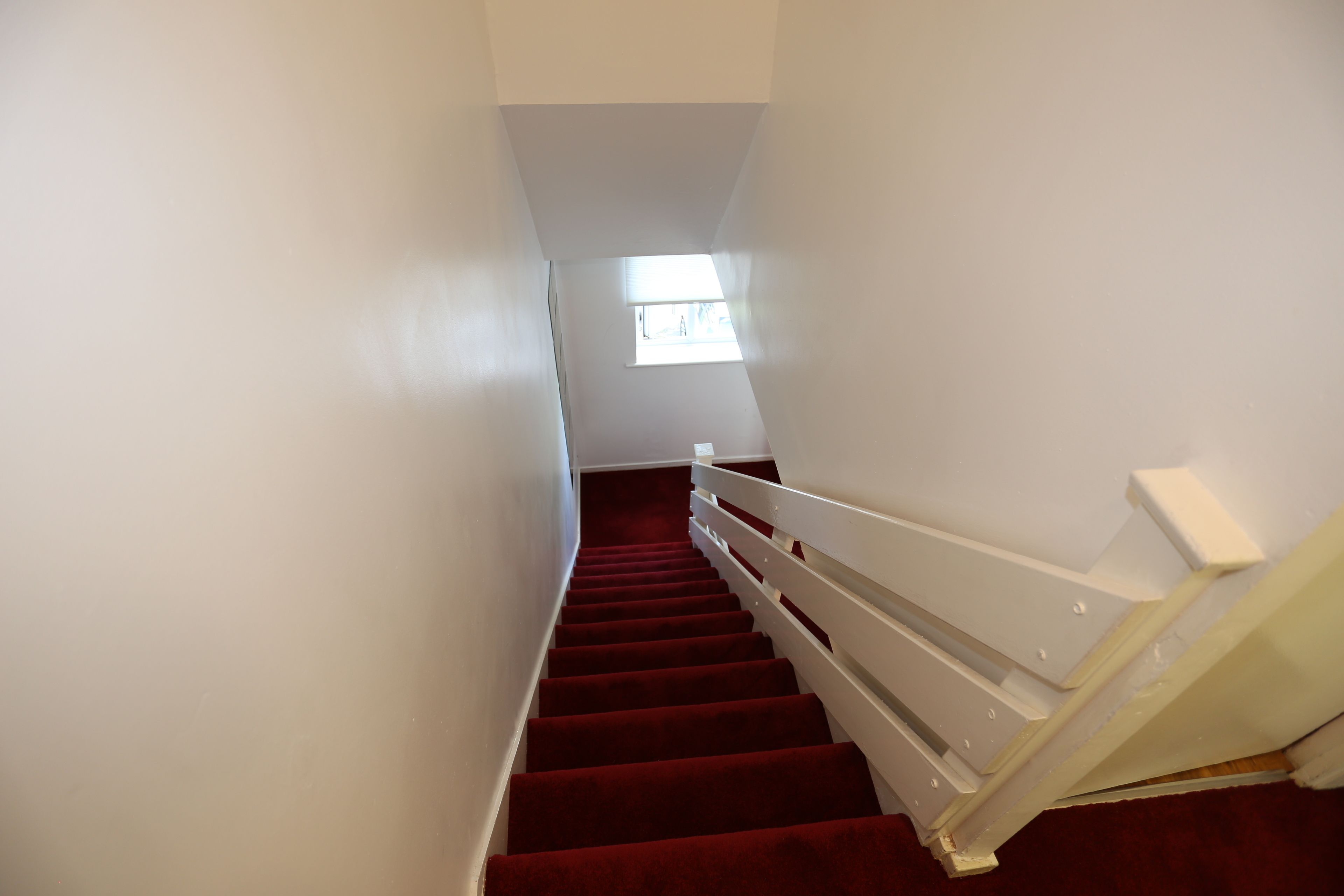 A staircase with red carpet and white railings leading to a landing with a window.