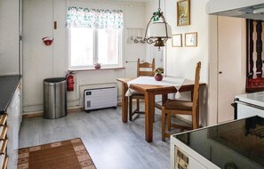 Ett kompakt kök med ett matbord, stolar, ett element och en hängande lampa.