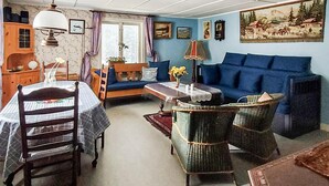 Ein gemütliches Wohnzimmer mit einem blauen Sofa, Korbstühlen, einem Holztisch und einem Bücherregal.