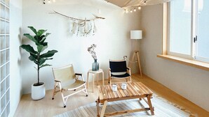A cozy room with a large potted plant, two chairs, a small table, and a lamp. - Hostel Tomato (Jiaoxi)