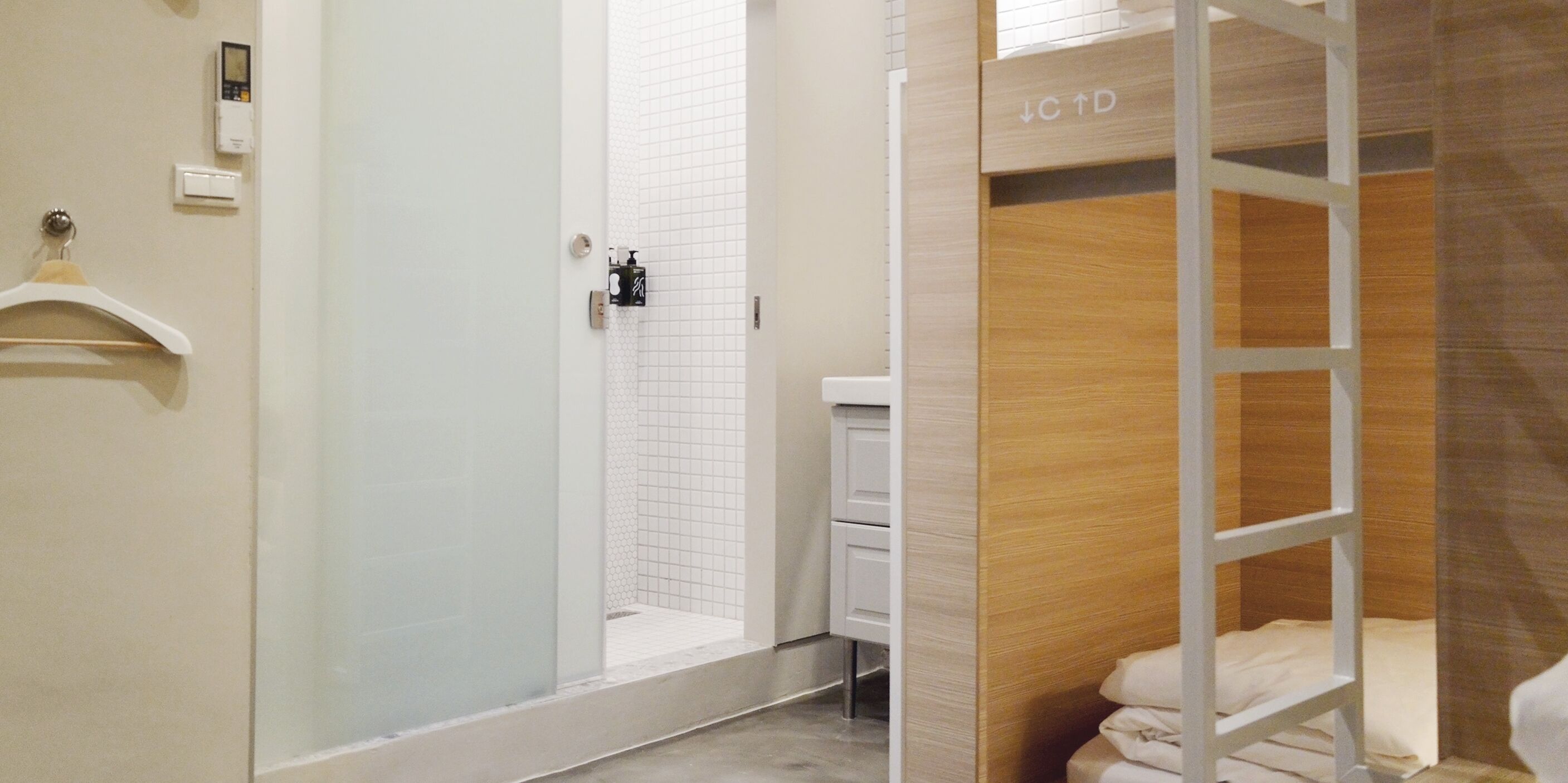 A modern bathroom with a glass shower enclosure, a wooden vanity, and a bunk bed with a sign indicating "C+D".