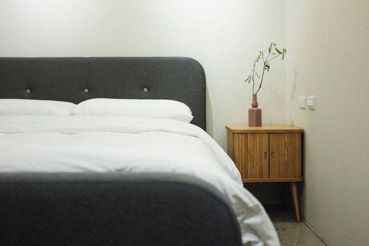 A bedroom with a bed, a wooden nightstand, and a vase with a plant.