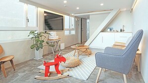 A modern living room with a high ceiling, a staircase, a kitchen area, and a large window providing natural light. - Hostel Tomato (Jiaoxi)