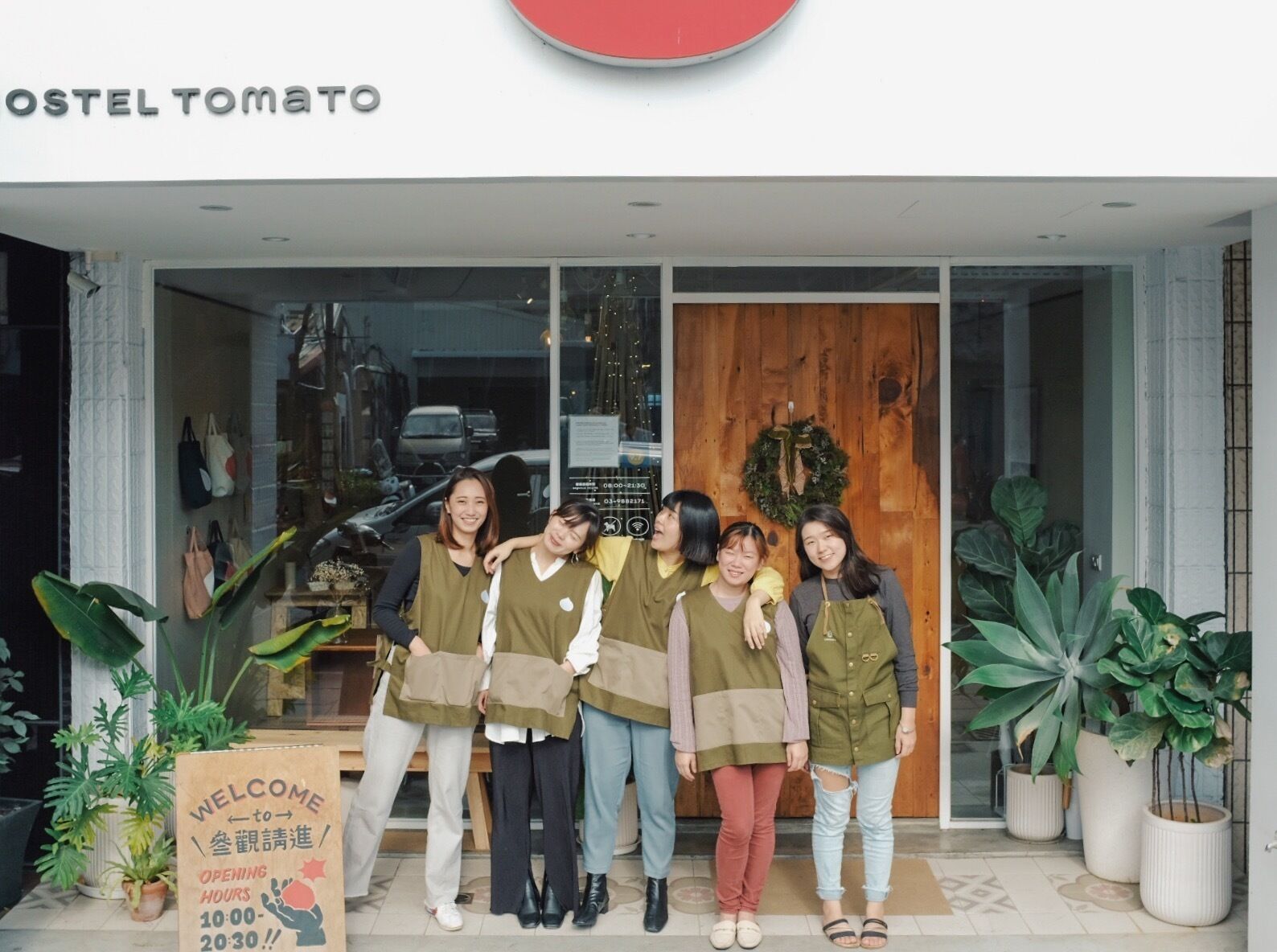 Un grupo de personas de pie frente a un edificio con un cartel que dice 'OSTEL TOMATO'.