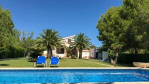 Ein Swimmingpool mit zwei blauen Liegestühlen, umgeben von Palmen und einem Gebäude im Hintergrund.