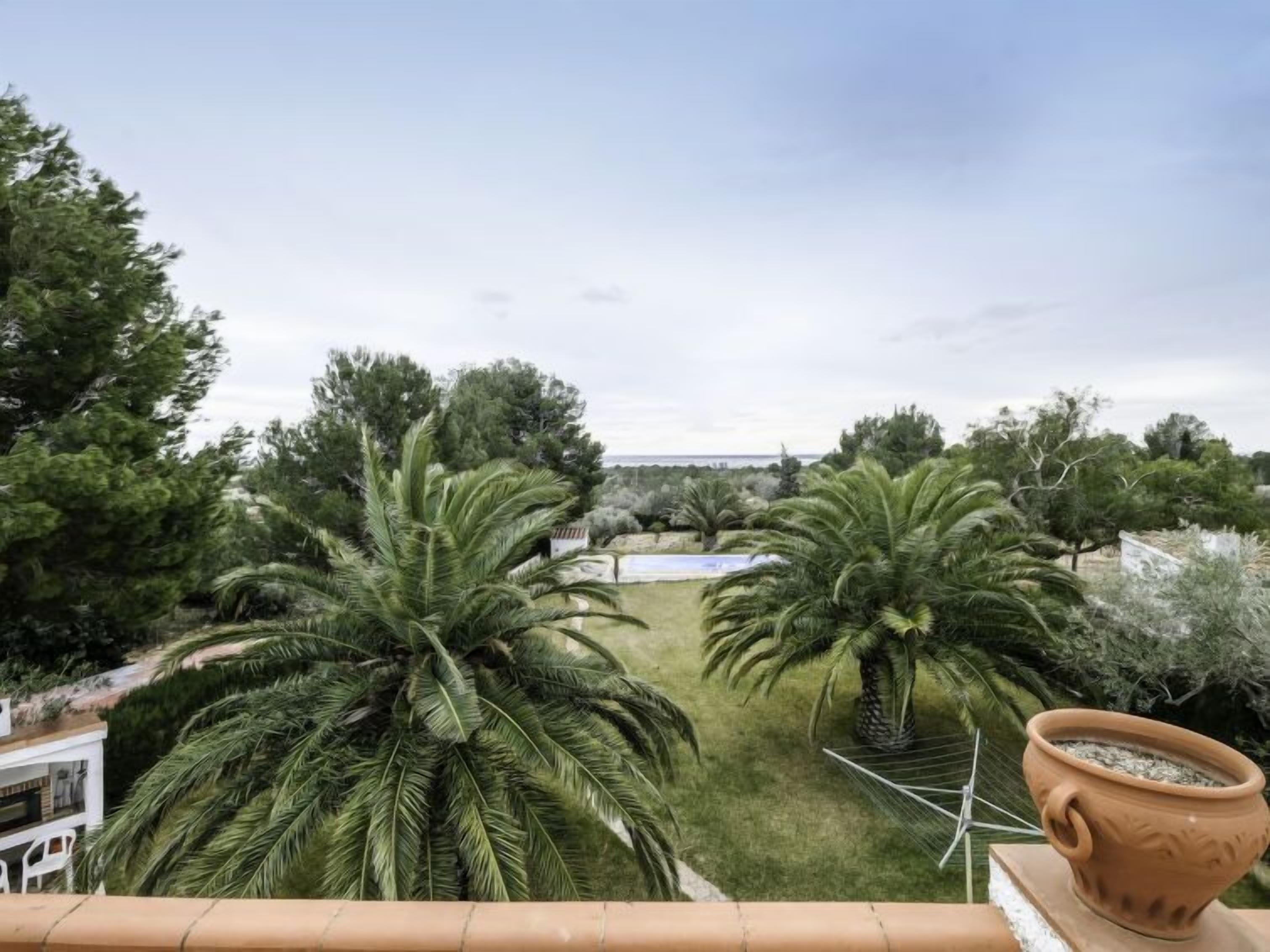 Una terraza con vistas a un jardín, que incluye palmeras y un edificio blanco.