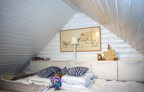 A bedroom with a sloped ceiling, a bed with white bedding, two pillows, a lamp, a framed picture on the wall, and a stuffed toy on the nightstand. - Beautiful home in Tidaholm with sauna (Tidaholm)