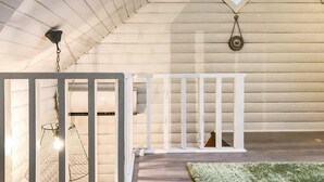 Une pièce avec un plafond en pente, une rambarde blanche, un luminaire suspendu et un puits de lumière.